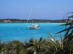 Serene Caribbean scene at Stingray Villa, Cozumel Mexico featuring a sailboat anchored in turquoise waters with lush coastal vegetation in the foreground.