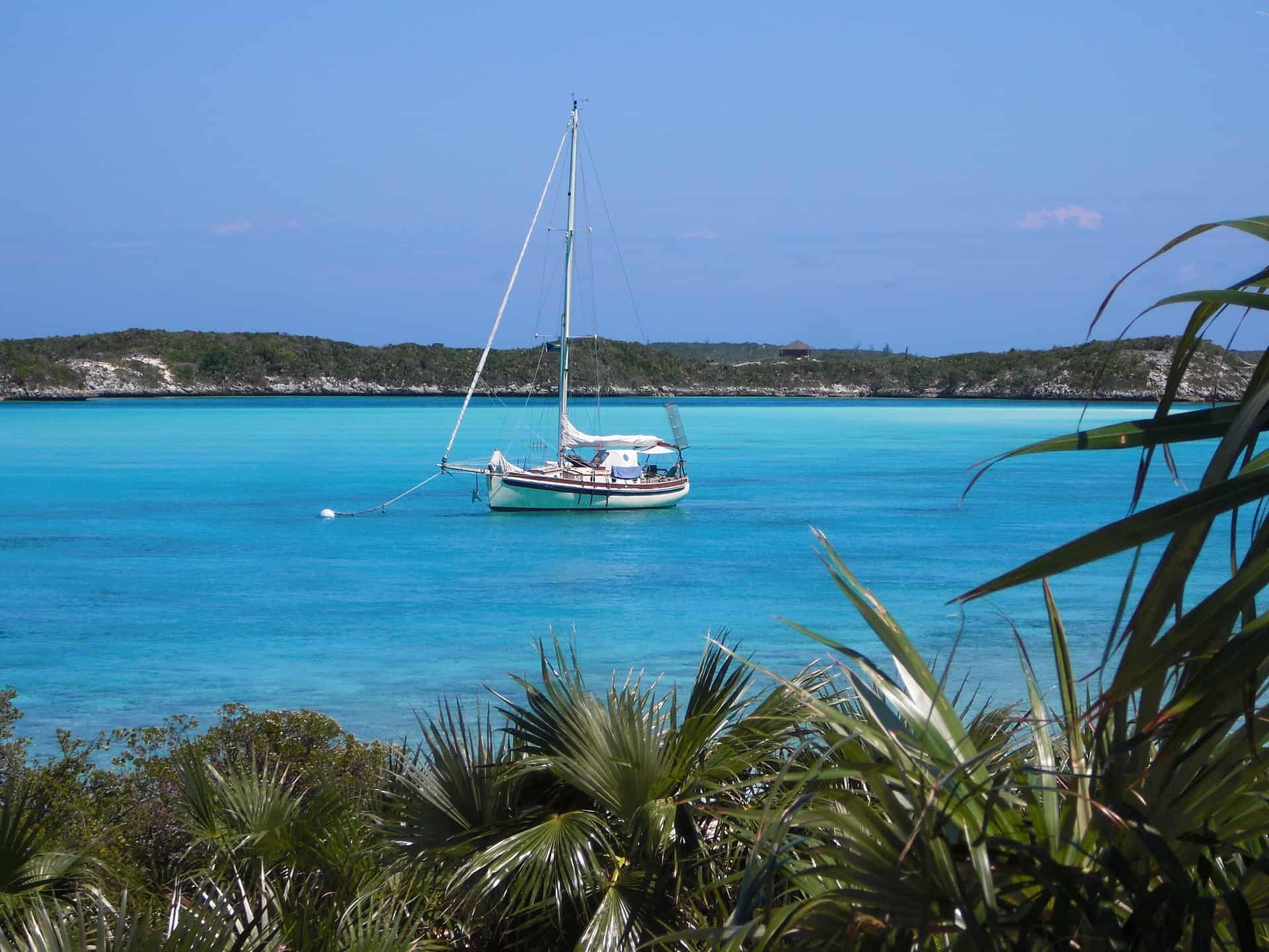 Serene Caribbean scene at Stingray Villa, Cozumel Mexico featuring a sailboat anchored in turquoise waters with lush coastal vegetation in the foreground.