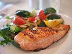 Freshly grilled salmon served with a side of mixed greens salad and lemon wedge, perfect for a healthy seafood meal at Cozumel.