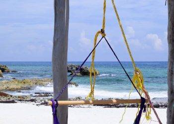Colorful hammock hanging on wooden posts overlooking a clear ocean beach with rocks, perfect for relaxation at Stingray Villa in Cozumel.
