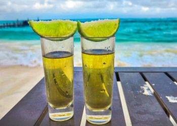 Refreshing tequila shots with lime wedges on a beachside table, perfect for relaxing by the ocean at Cozumel.