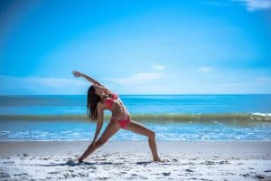 Relaxed woman practicing yoga on the sandy beach in Cozumel, Mexico, near Stingray Villa vacation rental, with crystal-clear ocean waters and blue sky in the background.