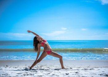 Relaxed woman practicing yoga on the sandy beach in Cozumel, Mexico, near Stingray Villa vacation rental, with crystal-clear ocean waters and blue sky in the background.