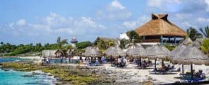 Brightly lit beachfront near Stingray Villa in Cozumel, Mexico, with traditional thatched-roof palapas, lounge chairs, and ocean views, ideal for relaxing vacations and exploring marine life.
