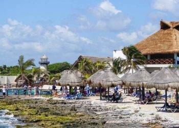 Brightly lit beachfront near Stingray Villa in Cozumel, Mexico, with traditional thatched-roof palapas, lounge chairs, and ocean views, ideal for relaxing vacations and exploring marine life.