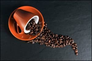 Coffee beans spilling from an orange cup on a black surface, representing the cozy atmosphere of Stingray Villa in Cozumel Mexico, perfect for coffee lovers and vacation relaxation.
