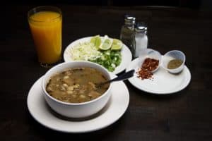 Fresh traditional Mexican soup with lime wedges, chili flakes, and herbs, served alongside juice and condiments, in Cozumel, Mexico.