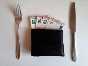 Euro banknotes inside a black wallet, placed between a fork and a knife, representing affordable vacation rentals at Stingray Villa in Cozumel Mexico.