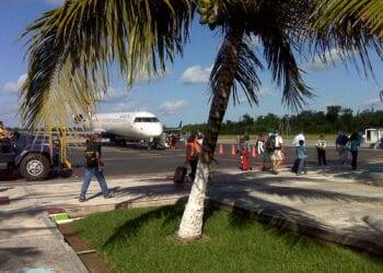 Aircraft on tarmac at Cozumel International Airport with travelers, palm tree in foreground, clear sky, and tropical scenery, offering a preview of the vacation experience near Stingray Villa.