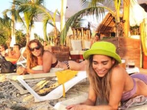 Vibrant Caribbean beach scene at Playa Casitas Beach in Cozumel, Mexico, showcasing relaxed guests sunbathing and enjoying tropical vibes under palm trees with beach loungers and colorful surroundings.