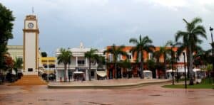 Colorful town square in Cozumel Mexico featuring a clock tower, palm trees, vibrant buildings, and lively local shops, perfect for vacation rentals at Stingray Villa.