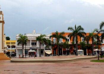 Colorful town square in Cozumel Mexico featuring a clock tower, palm trees, vibrant buildings, and lively local shops, perfect for vacation rentals at Stingray Villa.