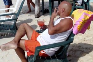 Relaxing man enjoying a cocktail on the beach in Cozumel, Mexico, while smoking a cigar in orange swim trunks.