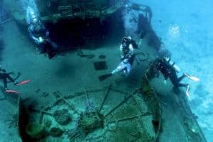 Colorful scuba divers exploring a C-53 shipwreck site off Cozumel, Mexico, part of Stingray Villa's underwater excursions. Experience vibrant marine life and underwater adventures in this popular vacation rental destination.