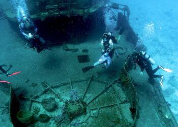 Colorful scuba divers exploring a C-53 shipwreck site off Cozumel, Mexico, part of Stingray Villa's underwater excursions. Experience vibrant marine life and underwater adventures in this popular vacation rental destination.