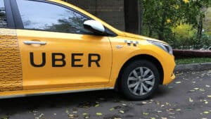 Uber taxi in Cozumel Mexico with vibrant yellow vehicle parked outdoors surrounded by autumn leaves and greenery.