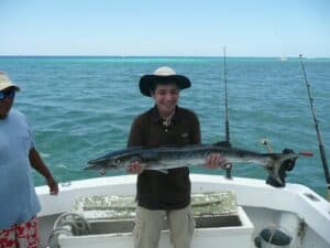 Vast ocean view with a smiling man holding a large fish on a boat in Cozumel, Mexico. Perfect for vacation rental and fishing adventure at Stingray Villa.