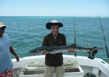 Vast ocean view with a smiling man holding a large fish on a boat in Cozumel, Mexico. Perfect for vacation rental and fishing adventure at Stingray Villa.