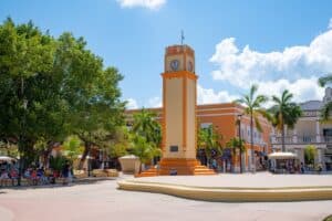 Colorful town square in Cozumel, Mexico with vibrant architecture, a clock tower, lush palm trees, and cultural charm, near Stingray Villa vacation rental.