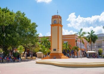 Colorful town square in Cozumel, Mexico with vibrant architecture, a clock tower, lush palm trees, and cultural charm, near Stingray Villa vacation rental.