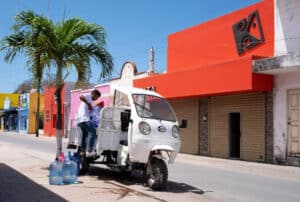 Colorful street scene in Cozumel Mexico with vibrant buildings and a traditional tuk-tuk vehicle delivering water. Exploring local life and culture near Stingray Villa vacation rental.