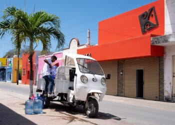 Colorful street scene in Cozumel Mexico with vibrant buildings and a traditional tuk-tuk vehicle delivering water. Exploring local life and culture near Stingray Villa vacation rental.