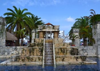 Lush tropical palm trees surround a decorative stone fountain in a tropical Puerta Maya Cozumel setting