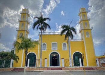 Colorful yellow church with twin bell towers and palm trees in tropical setting