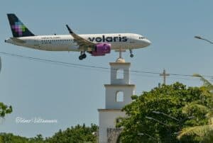 volaris airplane flying low over a church steeple in a tropical setting