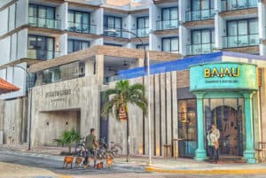 Modern hotel exterior with balconies and ocean view, featuring street-level restaurants.