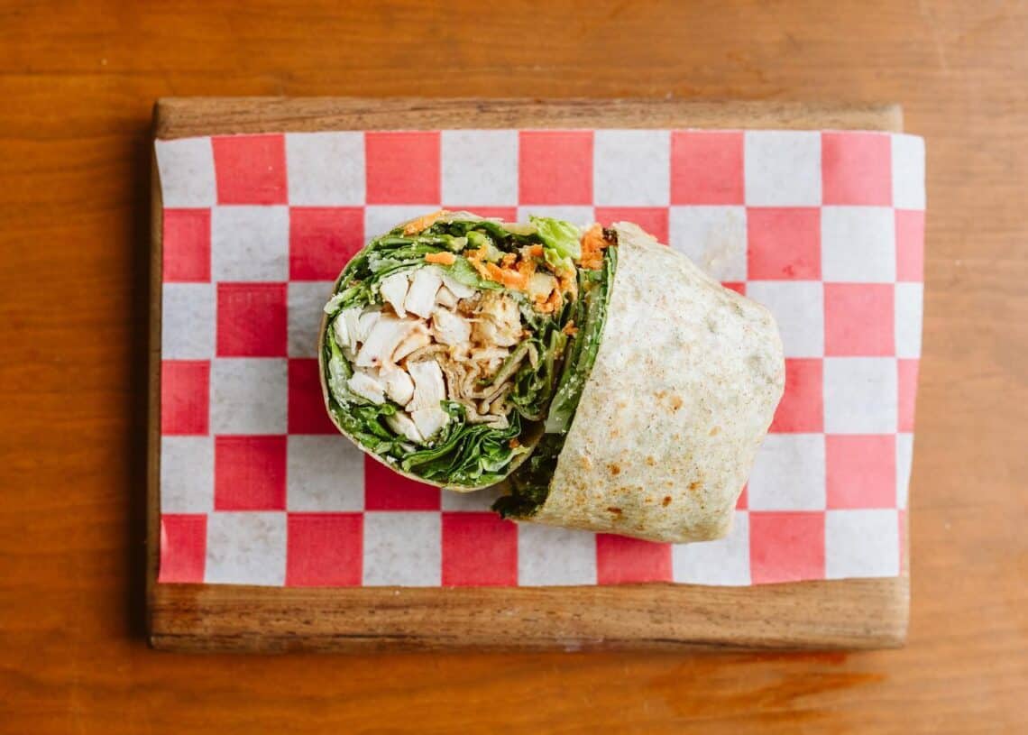 Fresh chicken wrap with lettuce, vegetables, and tortillas served on a wooden board, ideal for vacation dining at La Cuisine by Nutribalance in Cozumel, Mexico.
