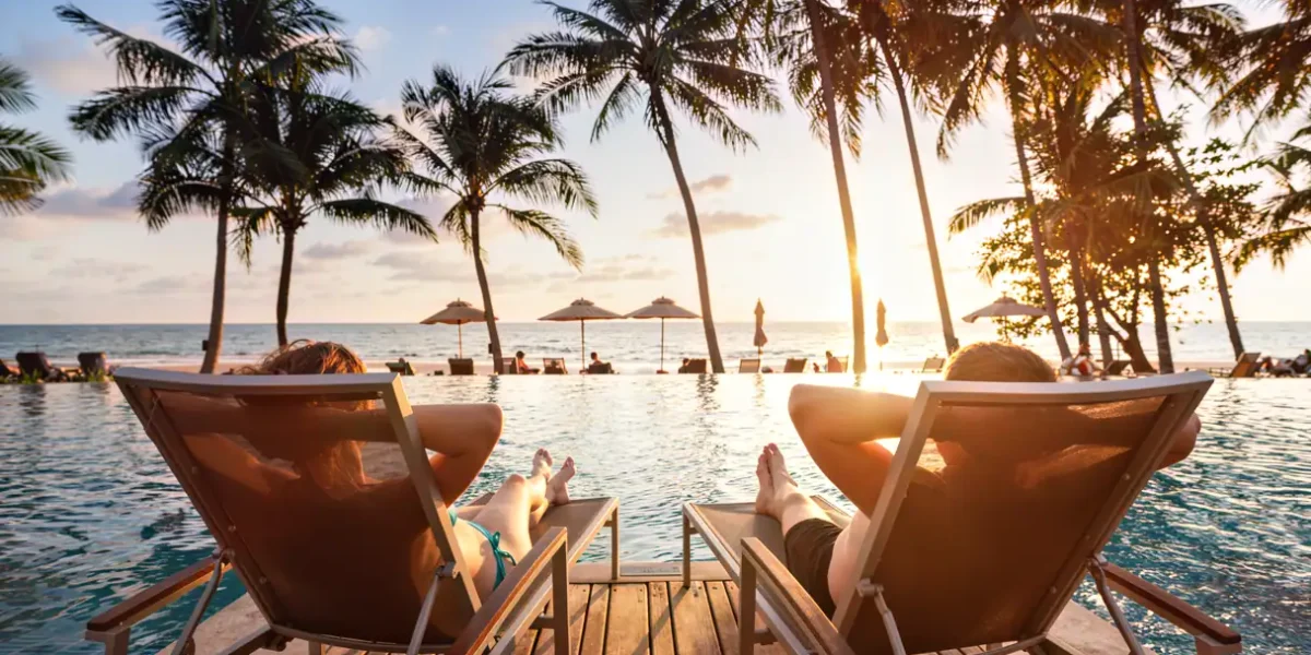 Relaxing poolside scene at Stingray Villa in Cozumel Mexico with two people lounging and palm trees at sunset.